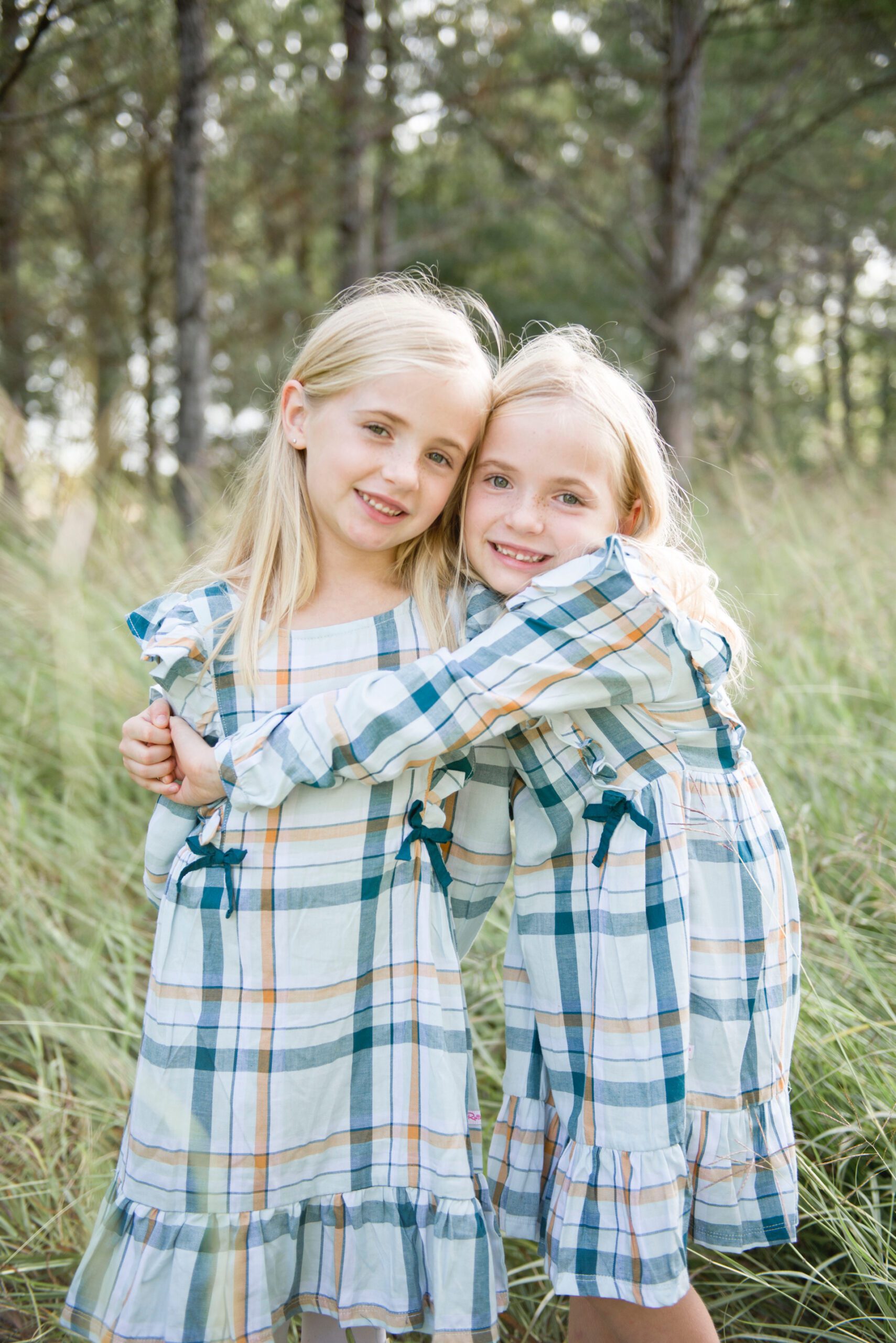 two blonde girls hugging in grassy field wearing dresses